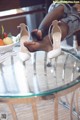 A woman sitting on top of a glass table next to a bowl of fruit.