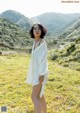 A woman standing in a grassy field with mountains in the background.