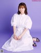 A woman in a white shirt dress sitting on a purple background.