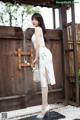 A woman in a white dress standing in front of a wooden gate.