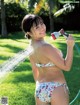 A woman in a bikini holding a hose in the grass.