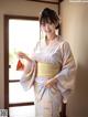 A woman in a kimono standing in front of a window.